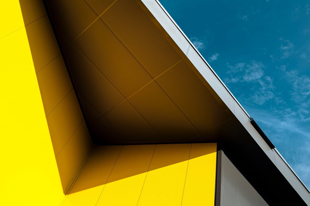 Edificio moderno amarillo y gris con superficie metálica bajo cielo azul